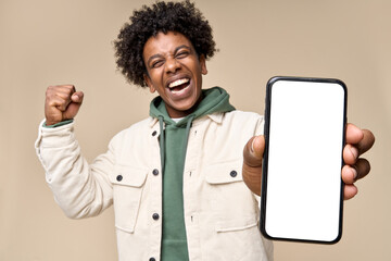 Happy African American teen student winner holding mobile cell phone winning on smartphone showing mock up big screen template presenting application, using cellphone isolated on beige background.