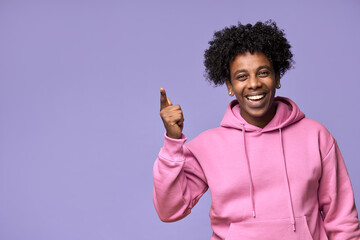 Wall Mural - Happy African American teen guy pointing fingers up advertising new promo offer. Smiling ethnic student model showing presenting ads or having great idea standing isolated on light purple background.