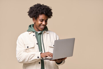 Wall Mural - Happy smiling African American teenager student holding laptop using computer technology presenting elearning, online education websites isolated on light beige background.