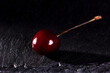 one red cherry with water drops on black stone background