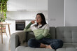 Concentrated pensive Asian girl student looks away and touches face with hand when planning trip to college. Carried away chinese woman sits on sofa in apartment thinking about university education