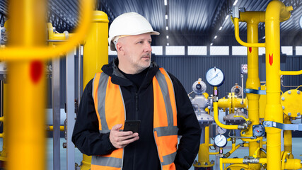 Poster - Man controls operation of boiler equipment. Yellow pipes inside industrial waste. Man with telephone in plants boiler room. Factory worker looks away. Working reflective vest and helmet