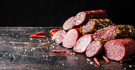 Poster - A variety of types of salami sausage with dried chili peppers on the table. 