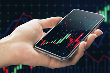 Wall Mural - Close up of female hand holding cellphone with glowing forex chart on blurry dark grid background. Trade, finance and invest concept.