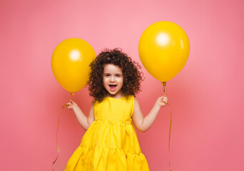 portrait of a cheerful little girl isolated on a pink background, holding a bunch of colorful balloo