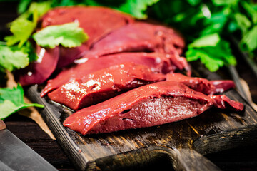 Fresh raw liver on a cutting board with parsley and a knife. 