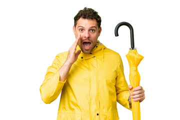 Wall Mural - Brazilian man with rainproof coat and umbrella over isolated chroma key background with surprise and shocked facial expression