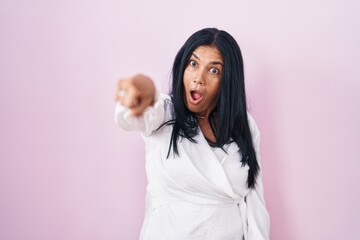 Sticker - Mature hispanic woman standing over pink background pointing with finger surprised ahead, open mouth amazed expression, something on the front