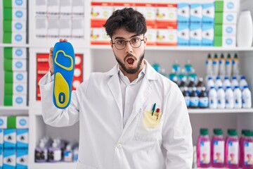 Canvas Print - Hispanic man with beard working at pharmacy drugstore holding insole scared and amazed with open mouth for surprise, disbelief face