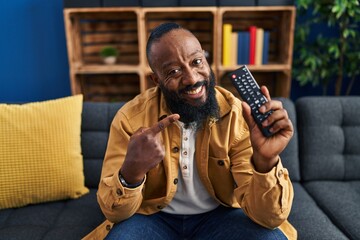 Poster - African american man holding television remote control smiling happy pointing with hand and finger