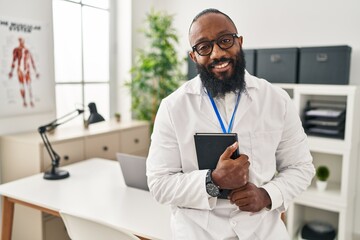 Sticker - Young african american man wearing doctor uniform holding book at clinic