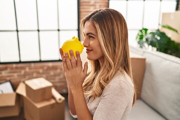 Wall Mural - Young blonde woman smiling confident holding piggy bank at new home