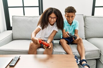 Canvas Print - Brother and sister playing video game sitting on sofa at home