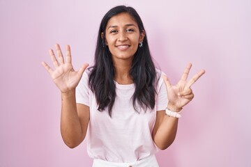 Sticker - Young hispanic woman standing over pink background showing and pointing up with fingers number eight while smiling confident and happy.