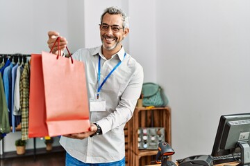 Sticker - Middle age grey-haired man shop assistant holding shopping bag at clothing store