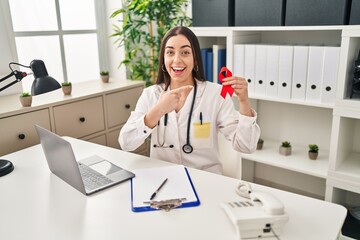 Poster - Hispanic doctor woman holding support red ribbon smiling happy pointing with hand and finger