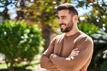 young hispanic man smiling confident standing with arms crossed gesture at park