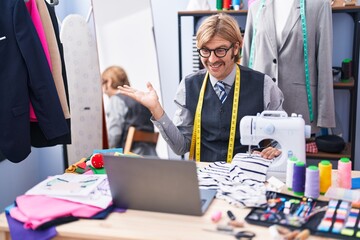 Canvas Print - Caucasian man with mustache dressmaker designer doing video call using sewing machine celebrating achievement with happy smile and winner expression with raised hand