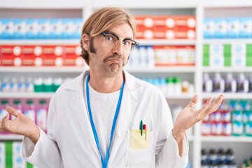 Canvas Print - Caucasian man with mustache working at pharmacy drugstore clueless and confused expression with arms and hands raised. doubt concept.