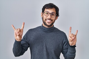 Poster - Handsome latin man standing over isolated background shouting with crazy expression doing rock symbol with hands up. music star. heavy music concept.