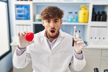 Poster - Arab man with beard working at scientist laboratory holding blood samples in shock face, looking skeptical and sarcastic, surprised with open mouth