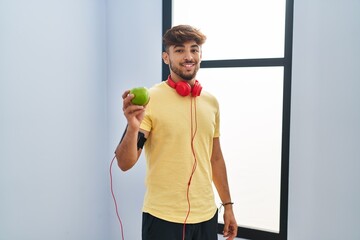 Sticker - Arab man with beard wearing sportswear eating green apple looking positive and happy standing and smiling with a confident smile showing teeth