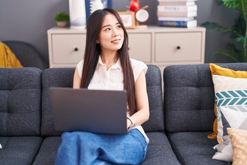 Poster - Young chinese woman using laptop sitting on sofa at home