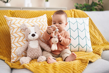 Sticker - Adorable hispanic toddler playing with toy sitting on sofa at home