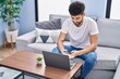 © Krakenimages.com - Young arab man using smartphone and laptop sitting on sofa at home