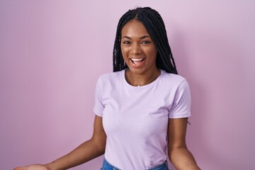 Sticker - African american woman with braids standing over pink background smiling cheerful with open arms as friendly welcome, positive and confident greetings