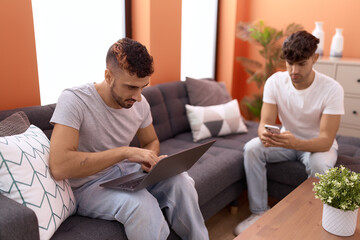 Sticker - Two hispanic men couple using laptop and smartphone sitting on sofa at home