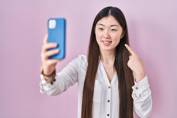 Canvas Print - Chinese young woman taking a selfie photo with smartphone smiling happy pointing with hand and finger