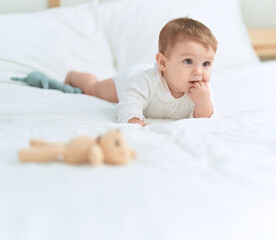 Adorable toddler lying on bed with teddy bear with serious expression at bedroom