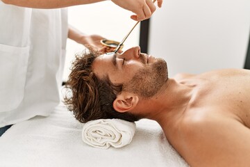 Poster - Young hispanic man having facial mask treatment at beauty center