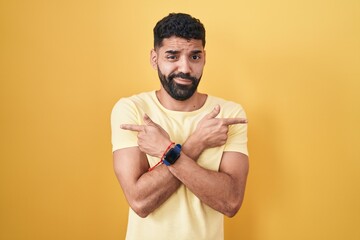 Wall Mural - Hispanic man with beard standing over yellow background pointing to both sides with fingers, different direction disagree