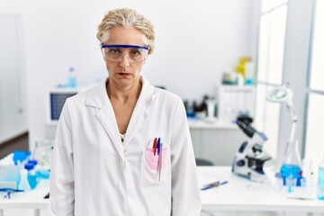 Poster - Middle age blonde woman working at scientist laboratory skeptic and nervous, frowning upset because of problem. negative person.