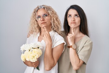 Poster - Mother and daughter holding bouquet of white flowers thinking concentrated about doubt with finger on chin and looking up wondering