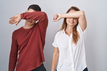 Sticker - Mother and son standing together over isolated background covering eyes with arm, looking serious and sad. sightless, hiding and rejection concept