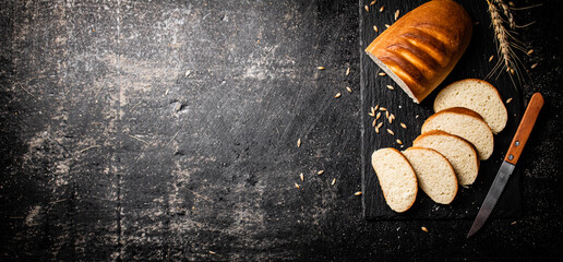 Poster - Sliced wheat bread with a knife on a stone board. 