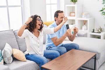 Wall Mural - Man and woman couple watching tv with winner expression at home