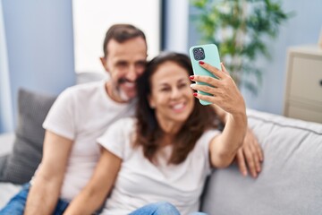 Wall Mural - Middle age man and woman couple make selfie by the smartphone sitting on sofa at home