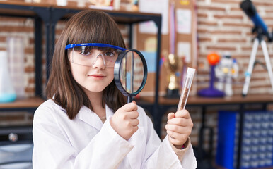 Poster - Adorable hispanic girl student looking test tube using magnifying glass at laboratory classroom