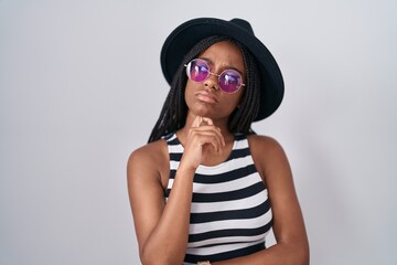 Wall Mural - Young african american with braids wearing hat and sunglasses with hand on chin thinking about question, pensive expression. smiling with thoughtful face. doubt concept.