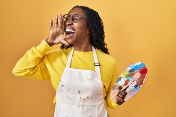 Canvas Print - African woman holding painter palette shouting and screaming loud to side with hand on mouth. communication concept.