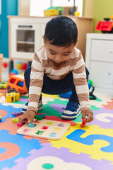 Wall Mural - Adorable hispanic toddler playing with maths puzzle game sitting on floor at kindergarten