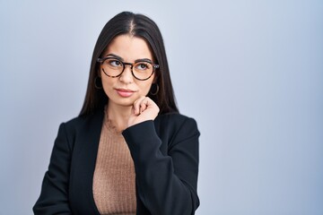 Sticker - Young brunette woman standing over blue background with hand on chin thinking about question, pensive expression. smiling with thoughtful face. doubt concept.