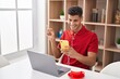 © Krakenimages.com - Young hispanic man using laptop and doing video call with smartphone smiling happy pointing with hand and finger to the side