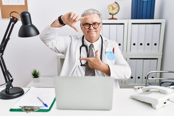 Poster - Senior caucasian man wearing doctor uniform and stethoscope at the clinic smiling making frame with hands and fingers with happy face. creativity and photography concept.