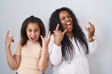 Sticker - Mother and young daughter standing over white background shouting with crazy expression doing rock symbol with hands up. music star. heavy music concept.