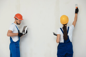 Wall Mural - Professional workers plastering wall with putty knives in hard hats